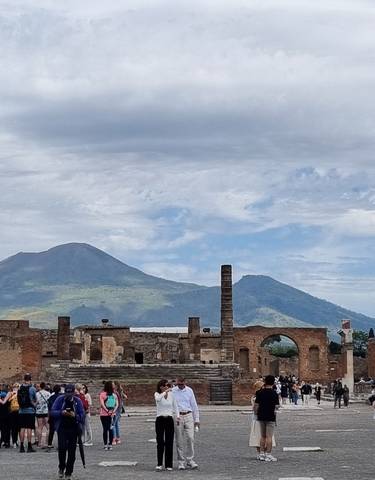 Ancient ruins with tourists and mountain backdrop.