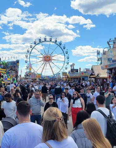 Crowded festival with fair rides under a clear sky.