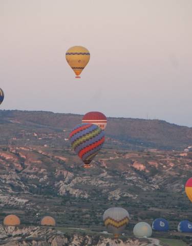 Hot air balloons floating over a scenic valley at sunrise.