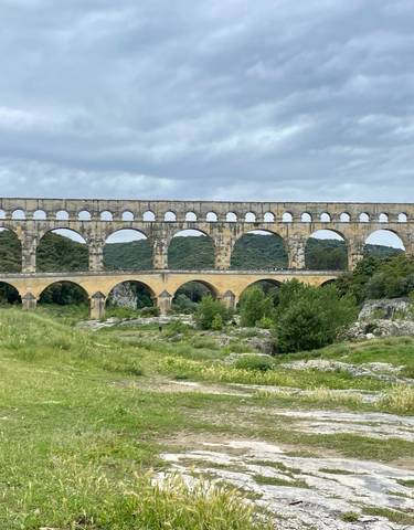 Ancient Roman aqueduct surrounded by greenery under a cloudy sky.