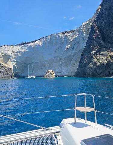A boat on clear blue water with a backdrop of rocky cliffs.