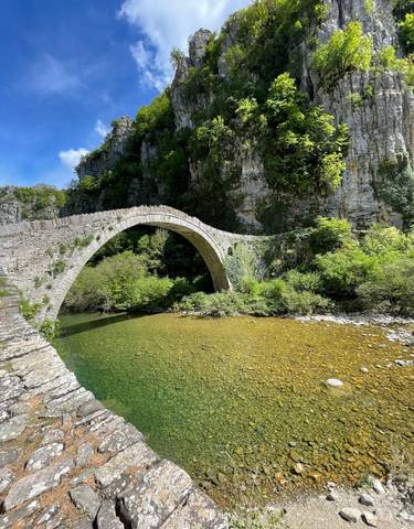 Stone arch bridge over a clear river surrounded by lush vegetation.