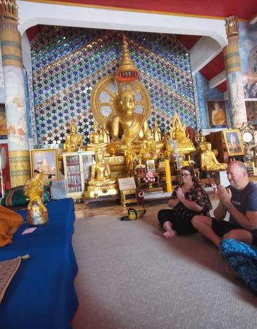 Monk leading a ceremony with people praying in a decorated temple.