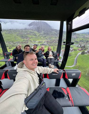 Group taking a selfie inside a cable car with mountains and village in the background.