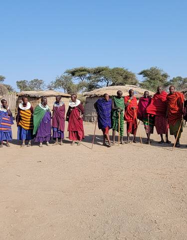 A line of traditionally dressed people in a rural setting with huts.