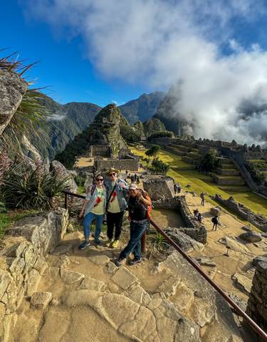Three people posing at Machu Picchu with ruins and mountains in the background.