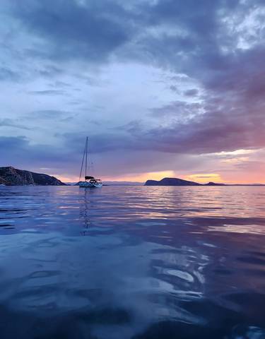 Sunset over the sea with sailboats and distant mountains.