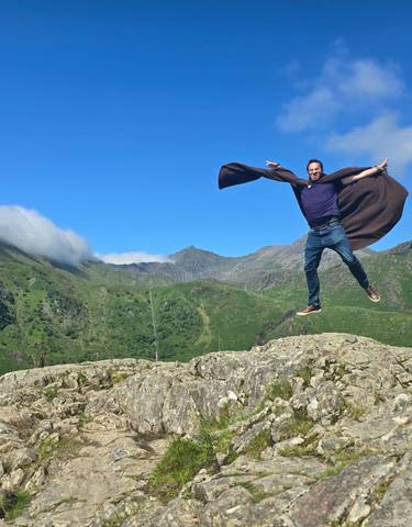 Man jumping on rocky terrain with mountains in the background.