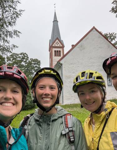 Four cyclists in front of a historic church on a rainy day.