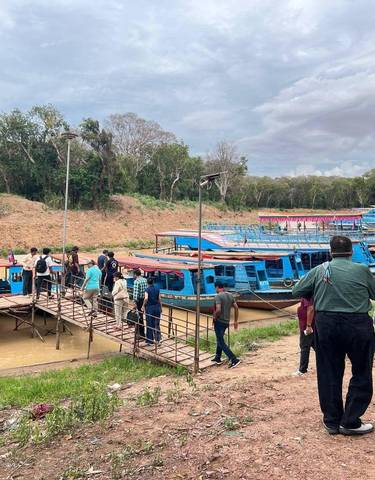 People boarding colorful boats at a riverbank, surrounded by lush greenery.