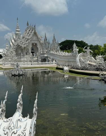 White intricately designed temple with a pond in front.