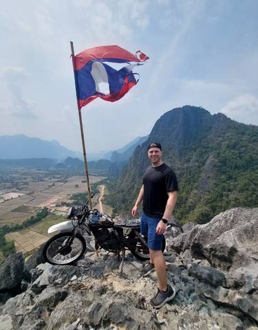 Traveler poses with a flag atop a hill offering panoramic views.