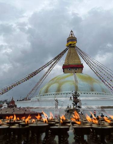 Boudhanath Stupa with prayer flags under cloudy sky.