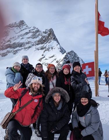 Group of people posing in snowy mountains with a Swiss flag.