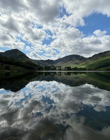 Serene lake with mountain reflections and cloudy sky.