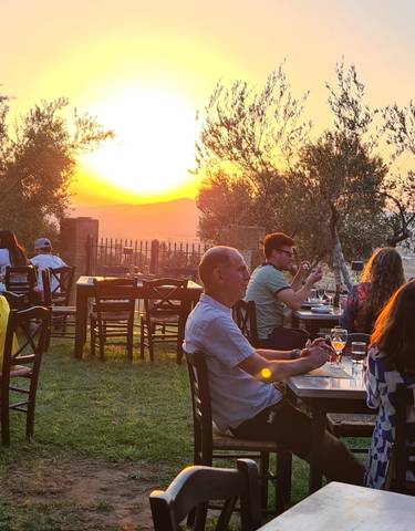 Open-air restaurant with people dining and watching the sunset over a hilly landscape.