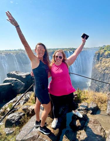 Two women celebrating with Victoria Falls in the background.