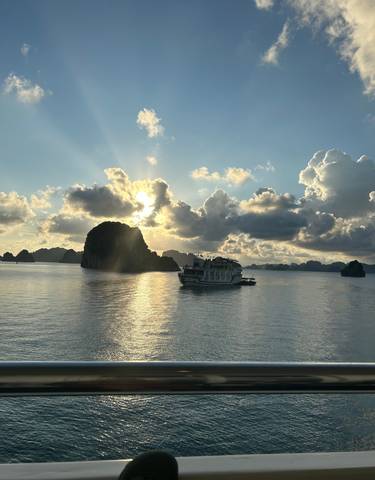 Boat cruising on a serene bay with limestone karsts during sunset.