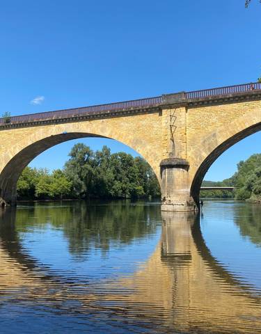 Stone bridge spanning over calm river waters amidst trees.