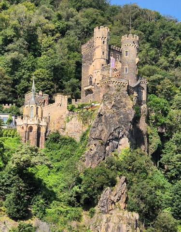 Castle built on rocky terrain surrounded by lush greenery.