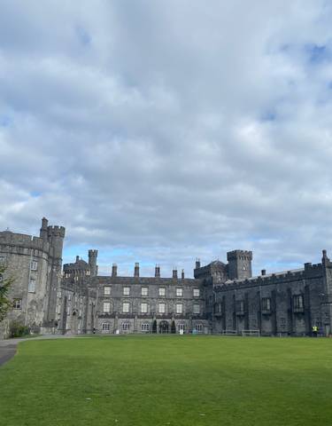 Imposing stone castle with bright green lawn and cloudy sky.