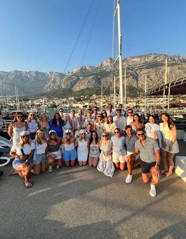Group of tourists in front of a harbor with mountains.
