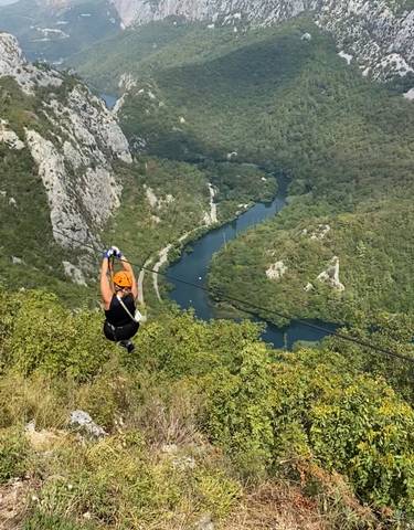 Person ziplining over a lush green valley with a river.