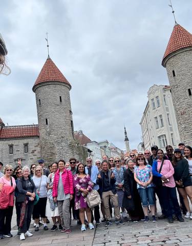 Group of people in front of historic stone buildings with towers.
