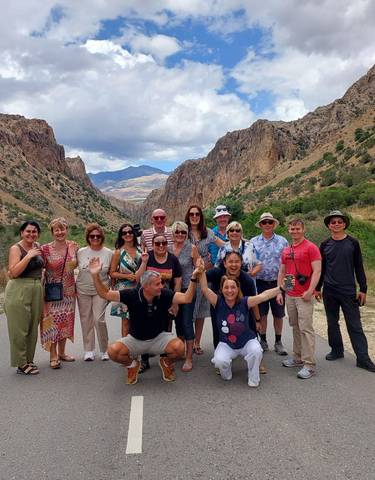 Group of tourists posing on a road with mountains in the background.