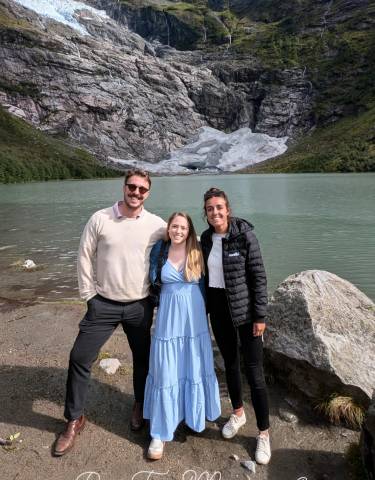 Three people posing with a glacier and lake in the background.