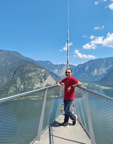 Man posing on a lookout with a scenic mountain and lake view.