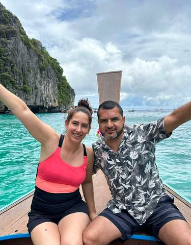 Two people waving on a boat with clear water and cliffs in the background.