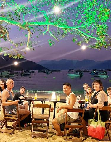 Group dining at the beach with boats in the background.