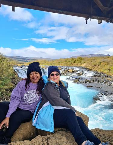 Two people smiling in front of a scenic waterfall.