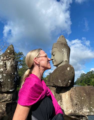 A person posing playfully with a stone statue at a historical site.
