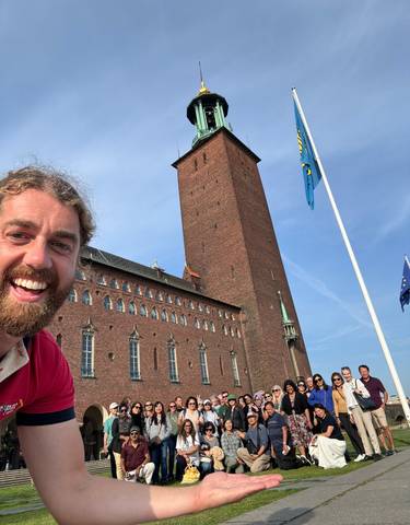 A smiling person in front of a large brick building.