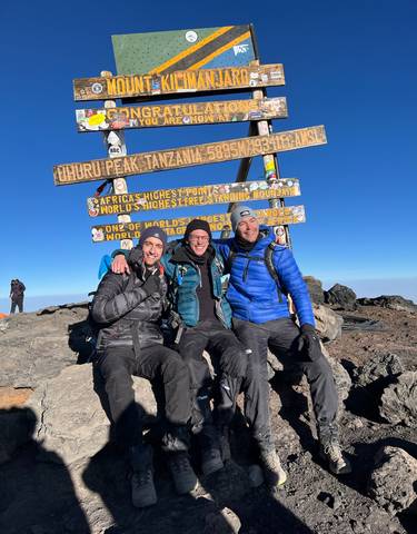 Three people posing at a sign that says 'Uhuru Peak, Tanzania'.
