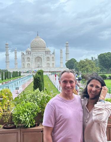 Couple smiling with the Taj Mahal in the background on a cloudy day.