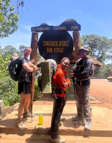Three people posing with hiking gear at a congratulatory sign.