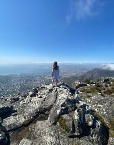 Person standing on the edge of a cliff overlooking a city and ocean.