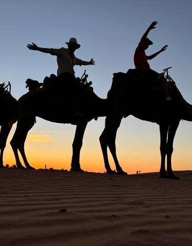 Silhouette of people riding camels at sunset.