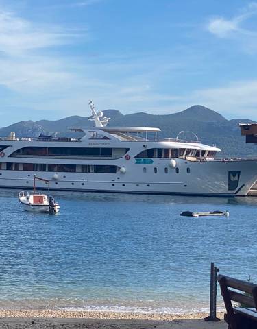 Large yacht moored in a harbor with mountains in the background.