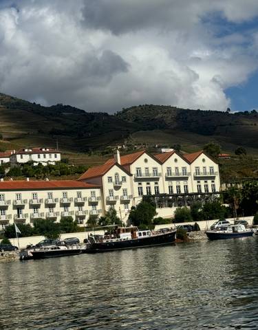 Scenic view of a river with buildings and terraced hills in the background.