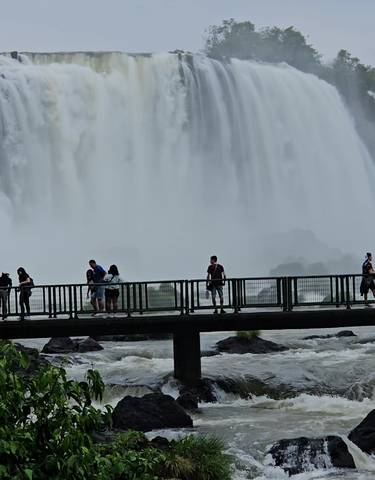 People walking on a viewing platform in front of a large waterfall.