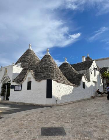 Traditional Trulli houses with conical roofs under a blue sky.