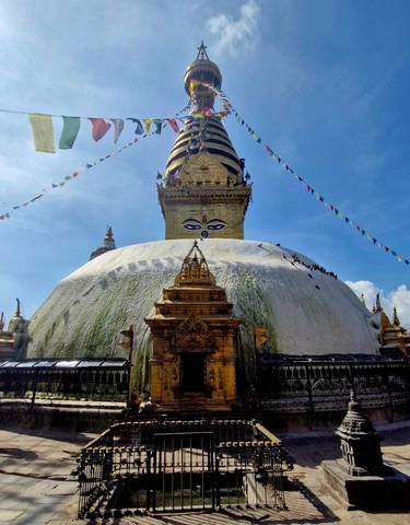 Large stupa with prayer flags against a blue sky.