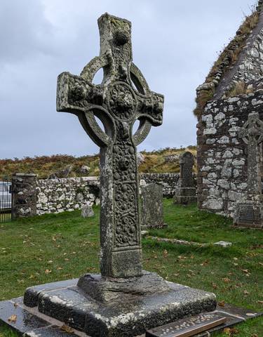 A historic stone Celtic cross in an ancient graveyard with a cloudy sky.