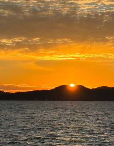 Sunset over the sea with hills silhouetted.