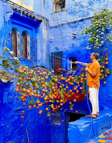 Man watering a tree in front of a blue wall with red fruit