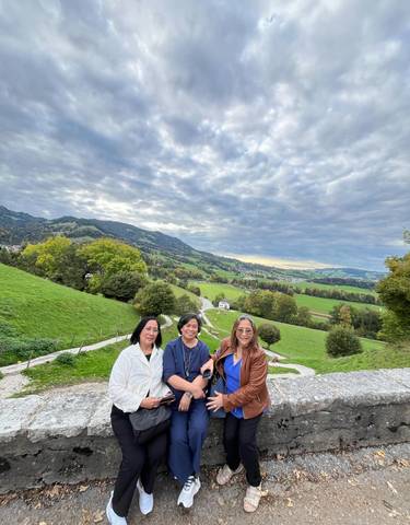 Three people posing in a green landscape with hills and a cloudy sky.